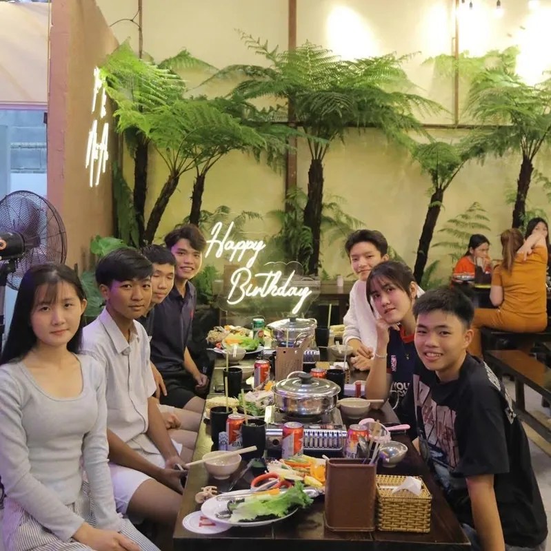 Nhóm bạn trẻ quây quanh bàn lẩu trong không gian cây xanh