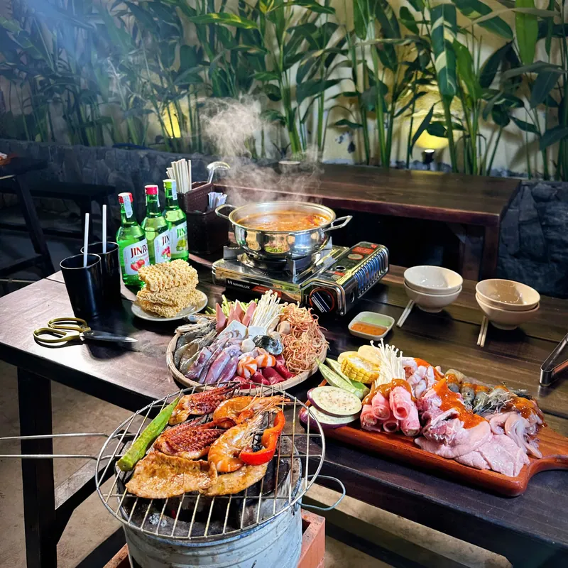 Toàn cảnh bàn lẩu nướng đầy đặn giữa khu cây xanh của quán