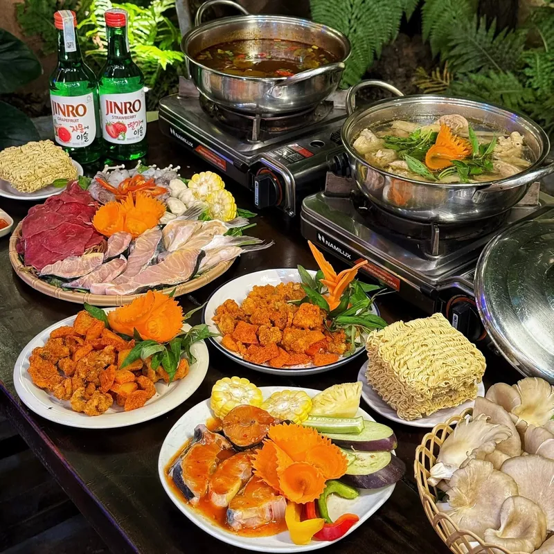 Hai nồi lẩu đang sôi trên bếp cùng mâm bò, cá, hải sản và các đĩa chả cá chiên