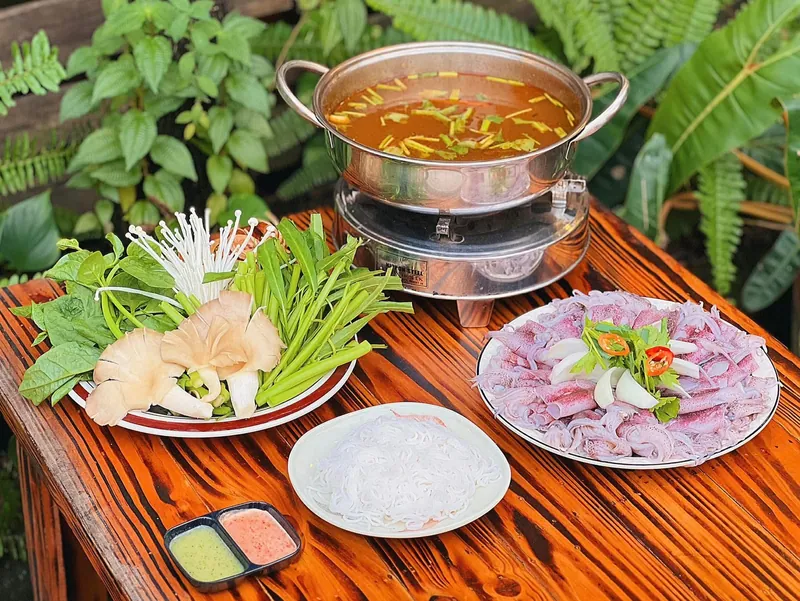 Nồi lẩu đang sôi cùng đĩa rau nấm tươi trên bàn gỗ